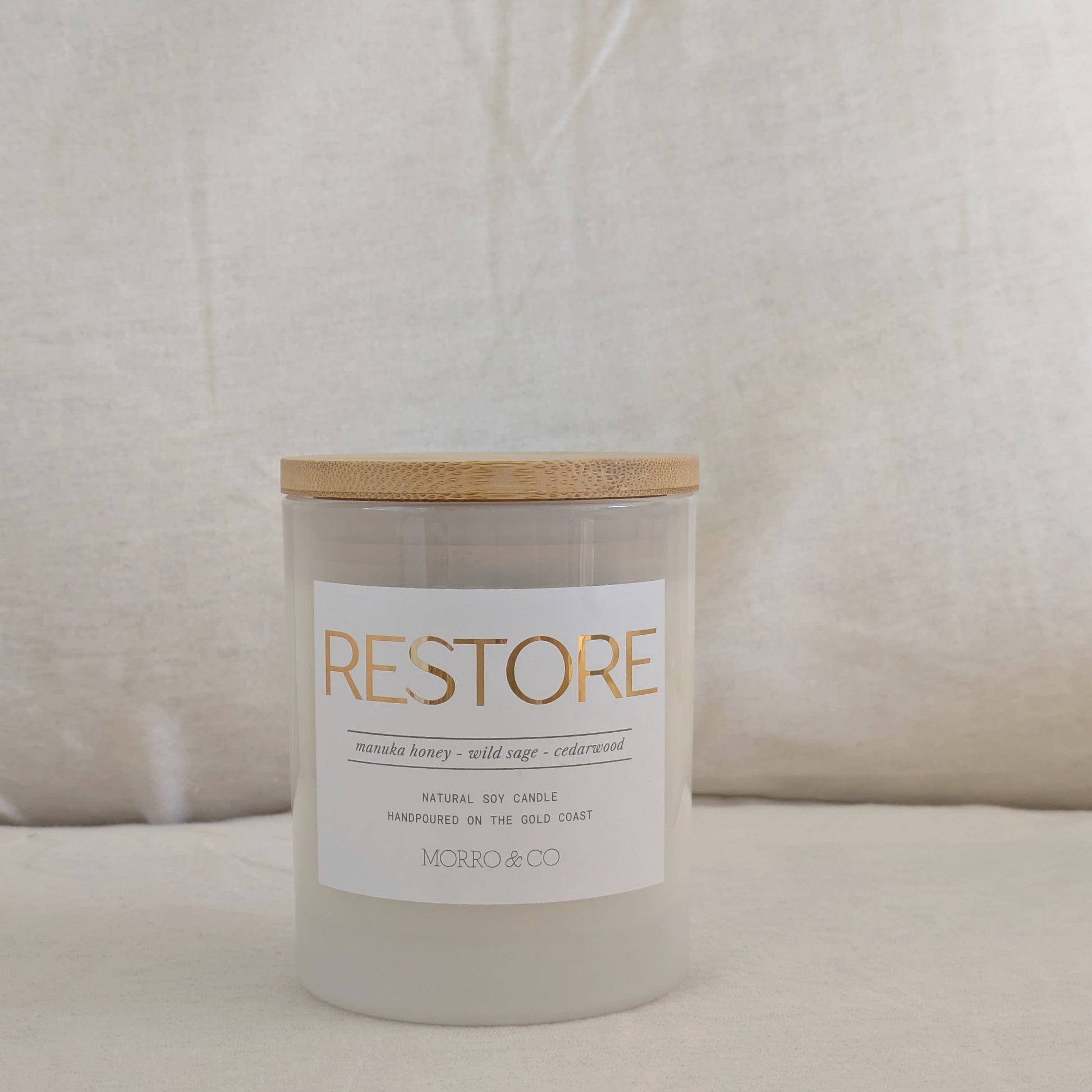 Candle labeled 'RESTORE' with gold label and wooden lid on a neutral background