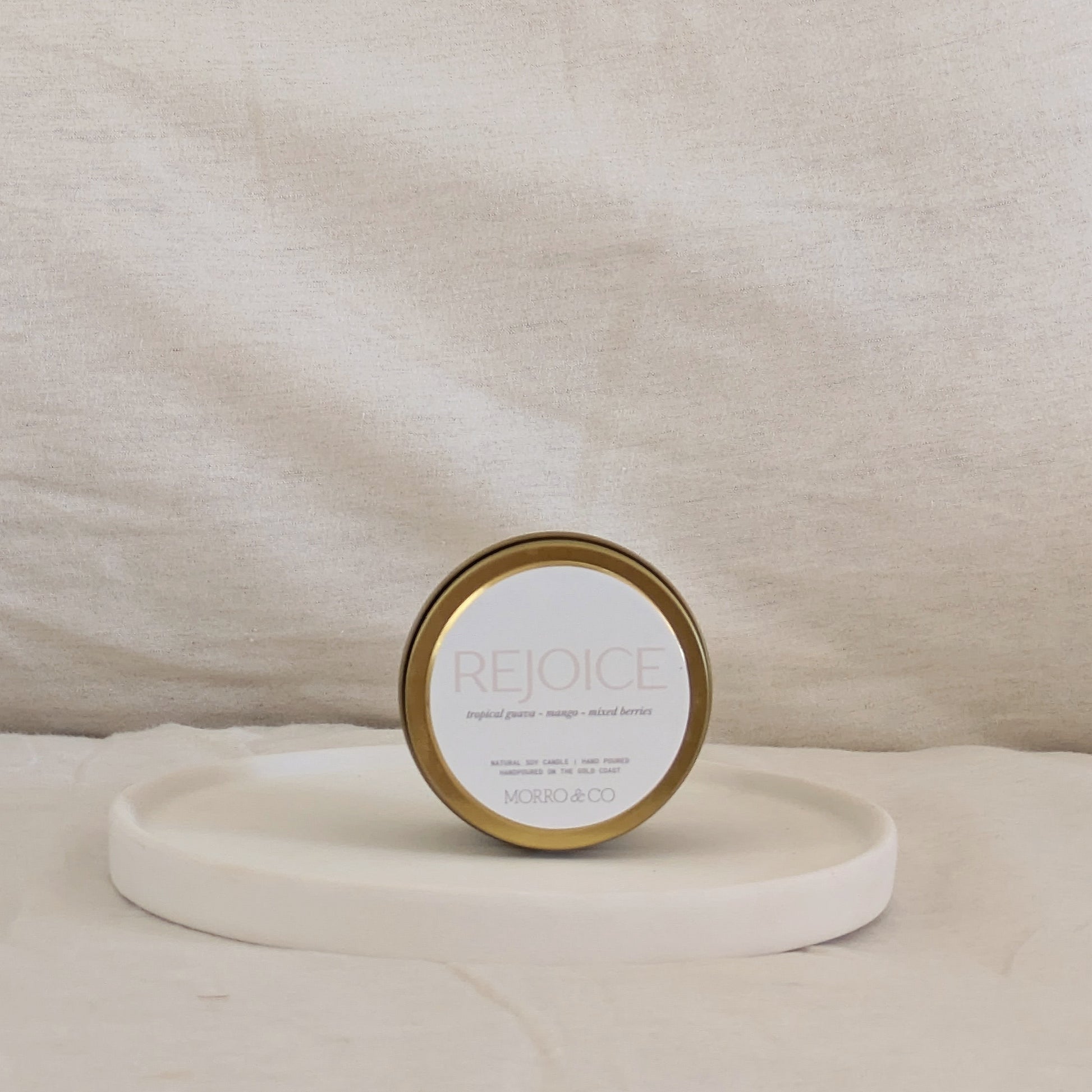 Gold candle travel tin 'Rejoice' on a beige surface