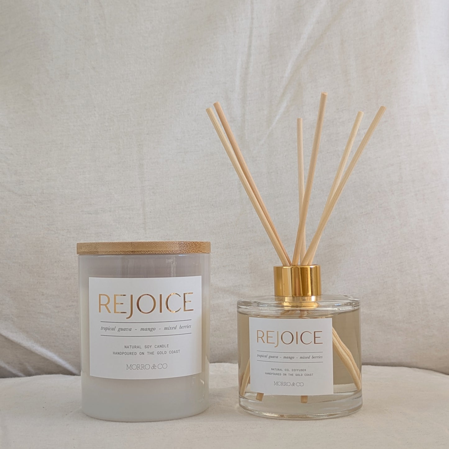 Two 'REJOICE' products, a candle and a diffuser, on a neutral background.