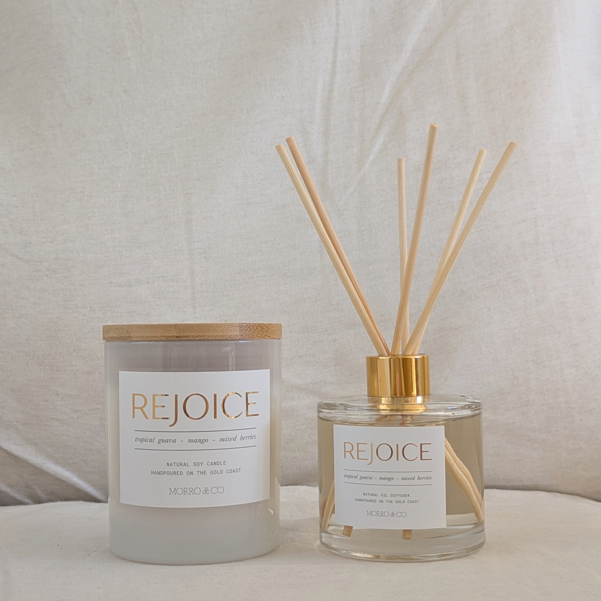 Two 'REJOICE' products, a candle and a diffuser, on a neutral background.
