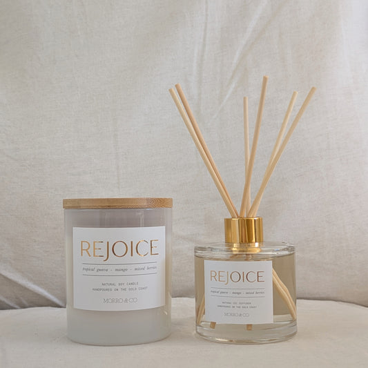 Two 'REJOICE' products, a candle and a diffuser, on a neutral background.