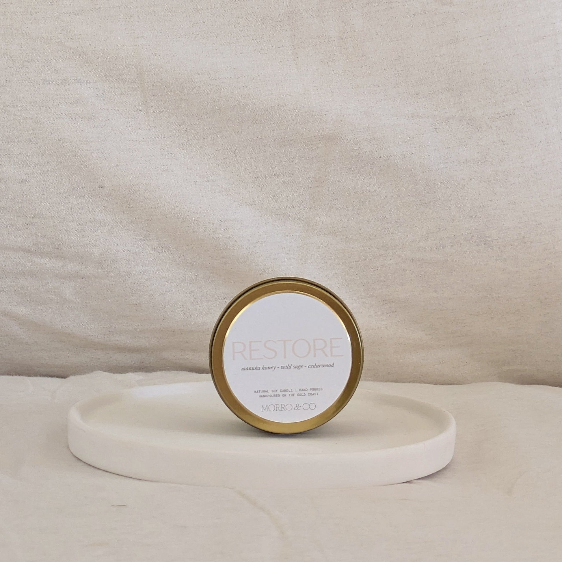 Candle gold travel tin labeled 'RESTORE' on a beige surface