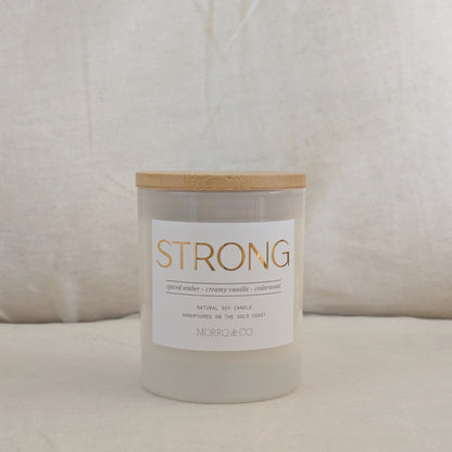 Candle labeled 'STRONG' with a wooden lid on a neutral background