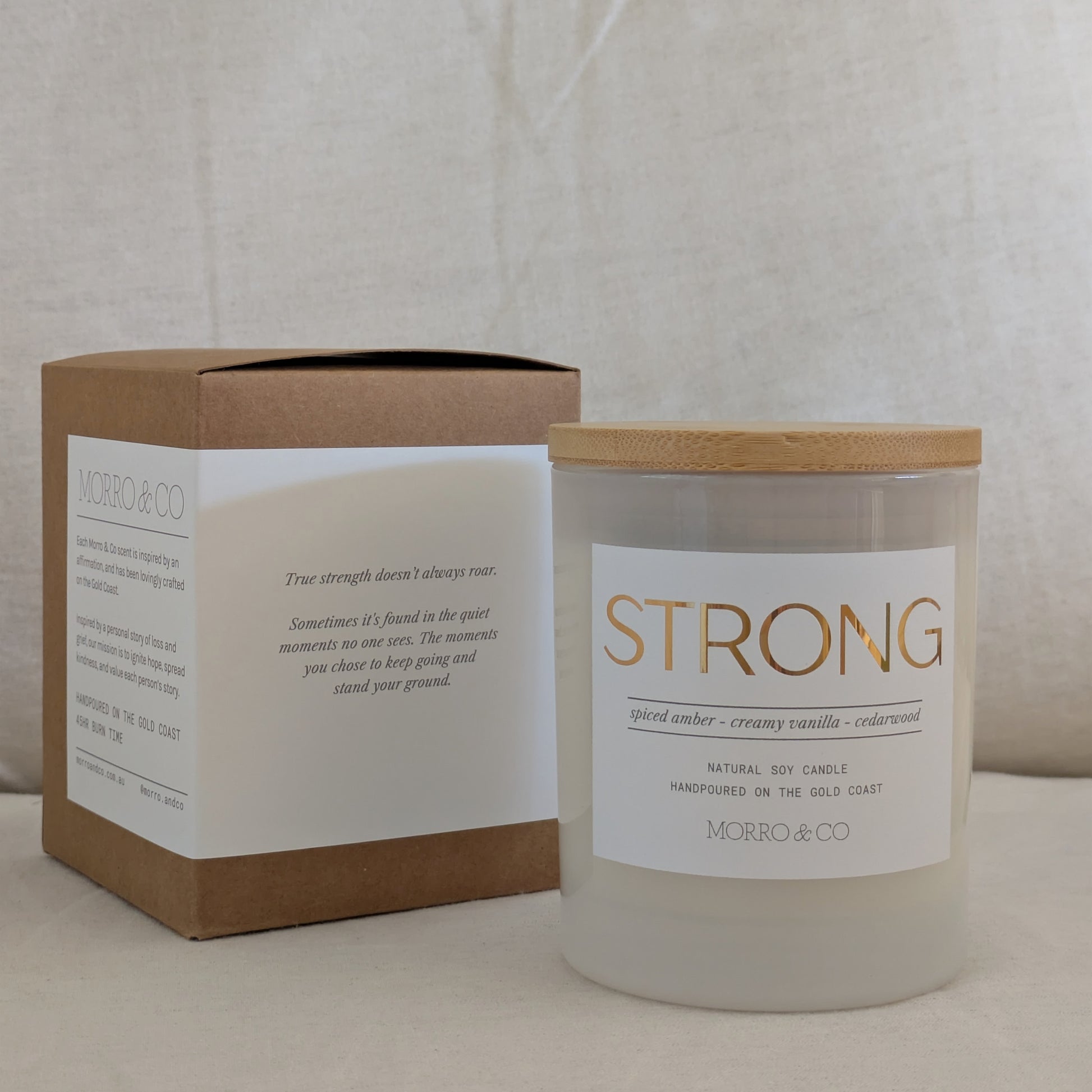 Gold labelled STRONG candle with wooden lid and packaging box on a neutral background