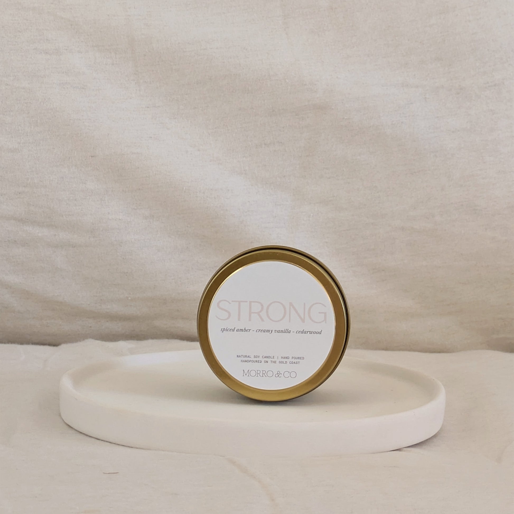 Gold candle travel tin labeled 'STRONG' on a beige surface
