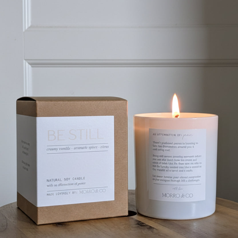 Be Still candle and packaging on a wooden surface with a neutral background