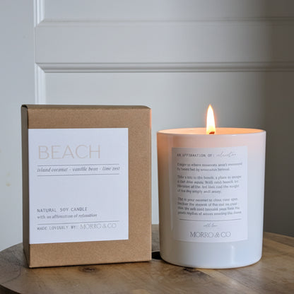 Candle and packaging labeled 'Beach' on a wooden surface with a neutral background