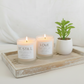 Two candles labeled 'Be Still' and 'Love' on a wooden tray with a small plant.