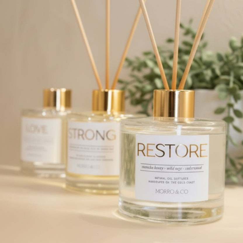 Three perfume bottles with gold caps and 'RESTORE' labels on a reflective surface.