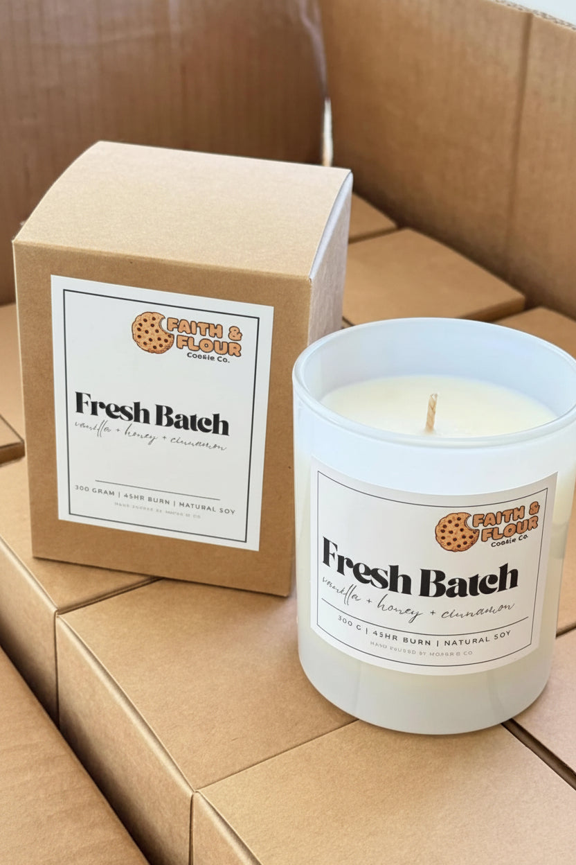 Candle labeled 'Fresh Batch' with packaging on a cardboard surface