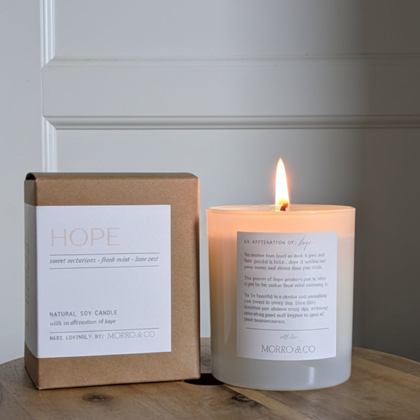 Candle and packaging labeled 'Hope' on a wooden surface with a neutral background