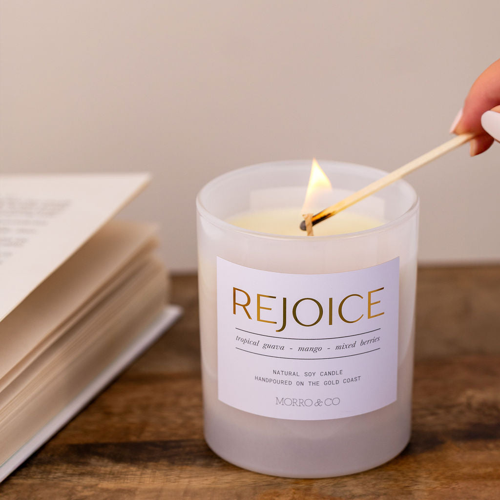 Candle being lit with a match, labeled 'Rejoice', on a wooden surface with an open book.