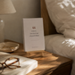 Morro & Co women's affirmation cards displayed on a wooden easel beside a bed.