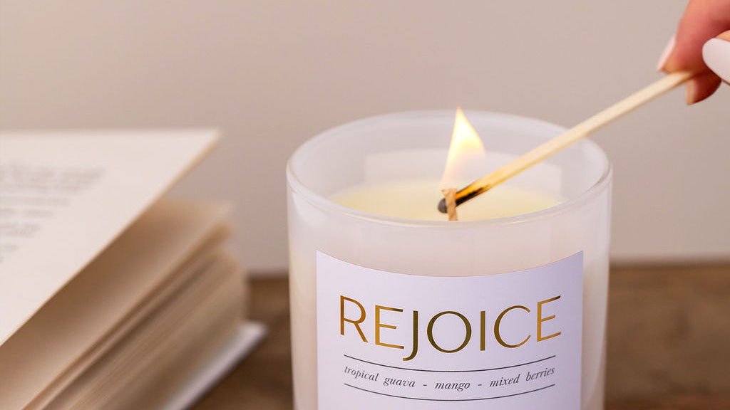 Candle being lit with a match, labeled 'Rejoice', on a wooden surface with an open book.