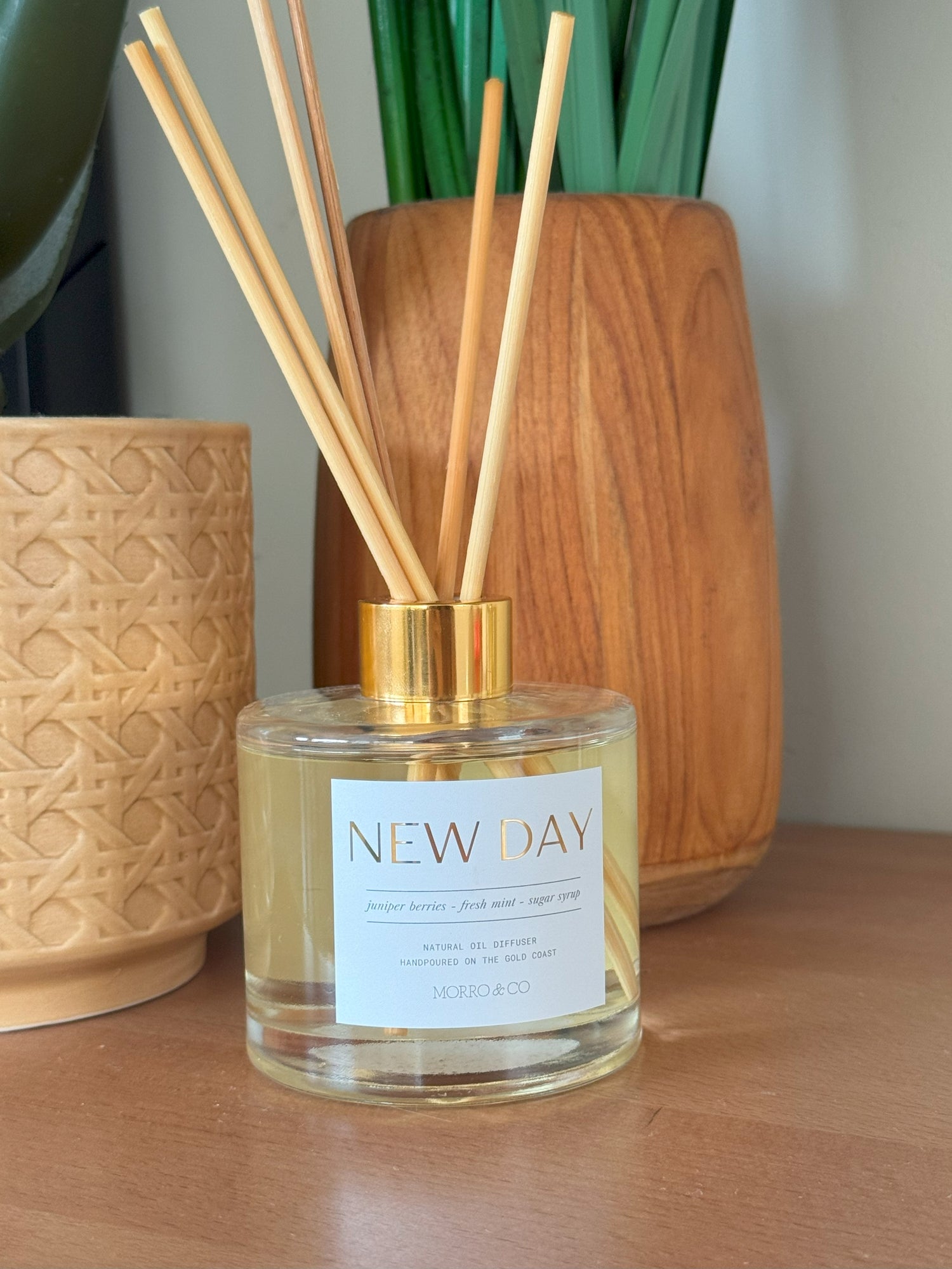 Diffuser bottle labeled 'New Day' with wooden sticks on a wooden surface.