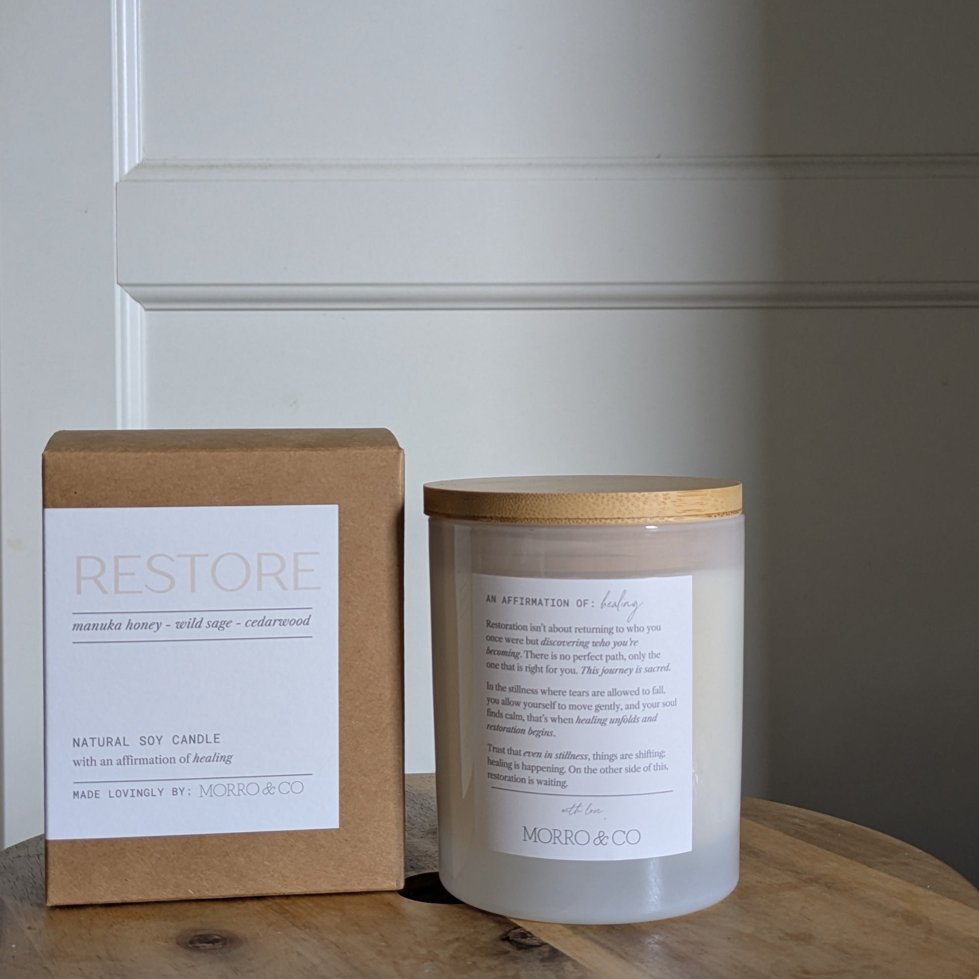 Candle and packaging labeled 'Restore' on a wooden surface with a neutral background