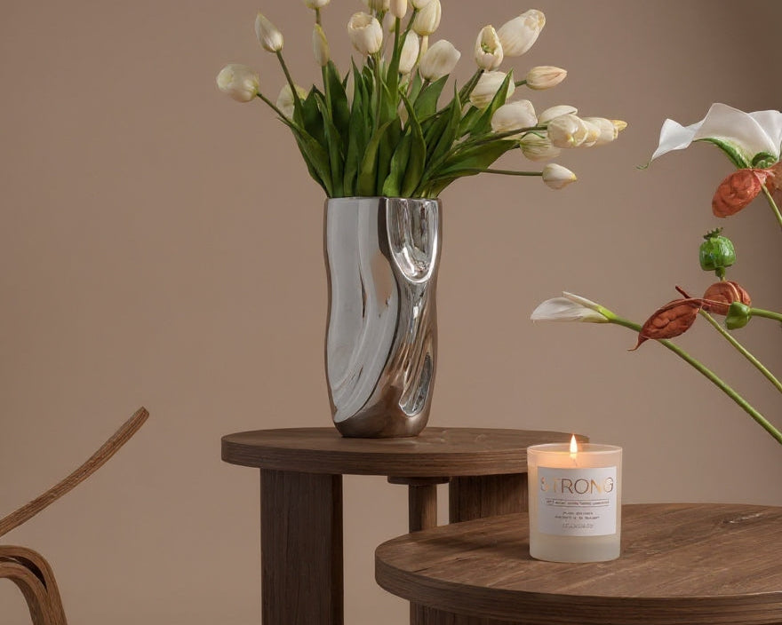 Wooden tables with a vase of white tulips and a lit candle on a neutral background