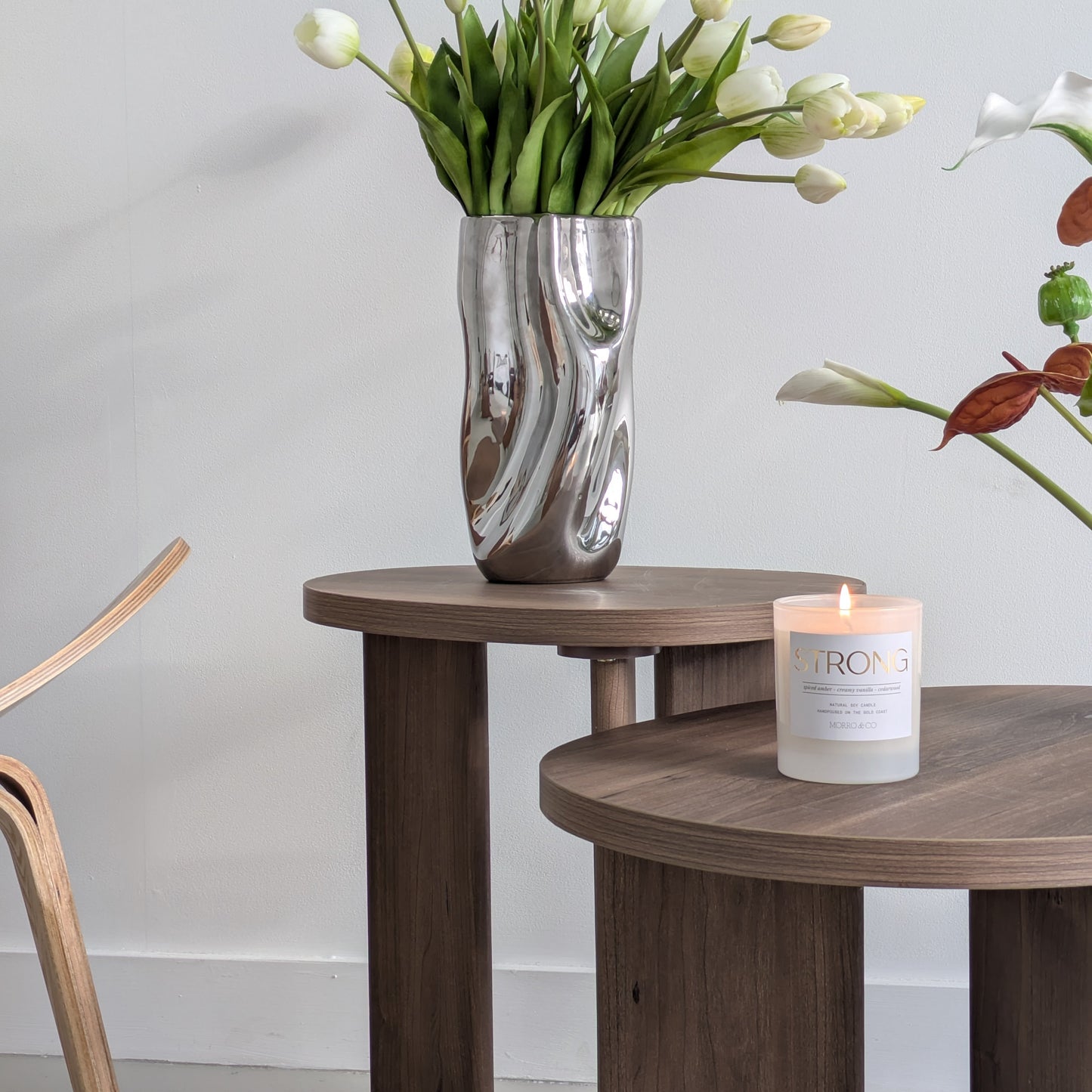 Wooden side table with a vase of white tulips and a candle on a light gray background