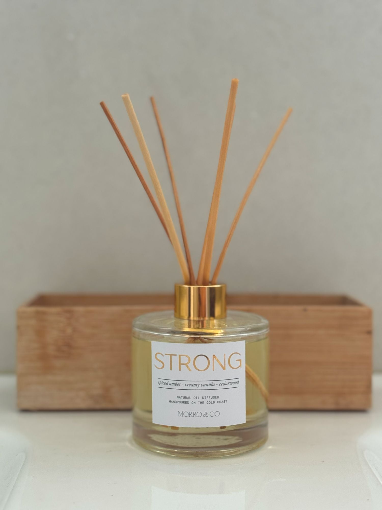 Reed diffuser labeled 'STRONG' with wooden sticks on a neutral background